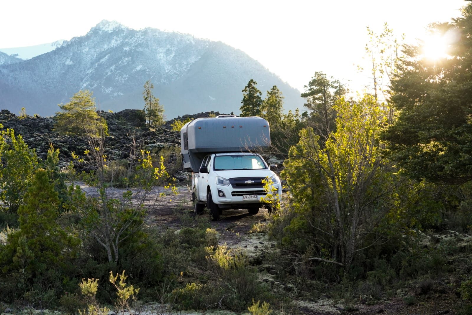 4x4 camper truck parked among trees with a snow-capped mountain behind, southern Chile