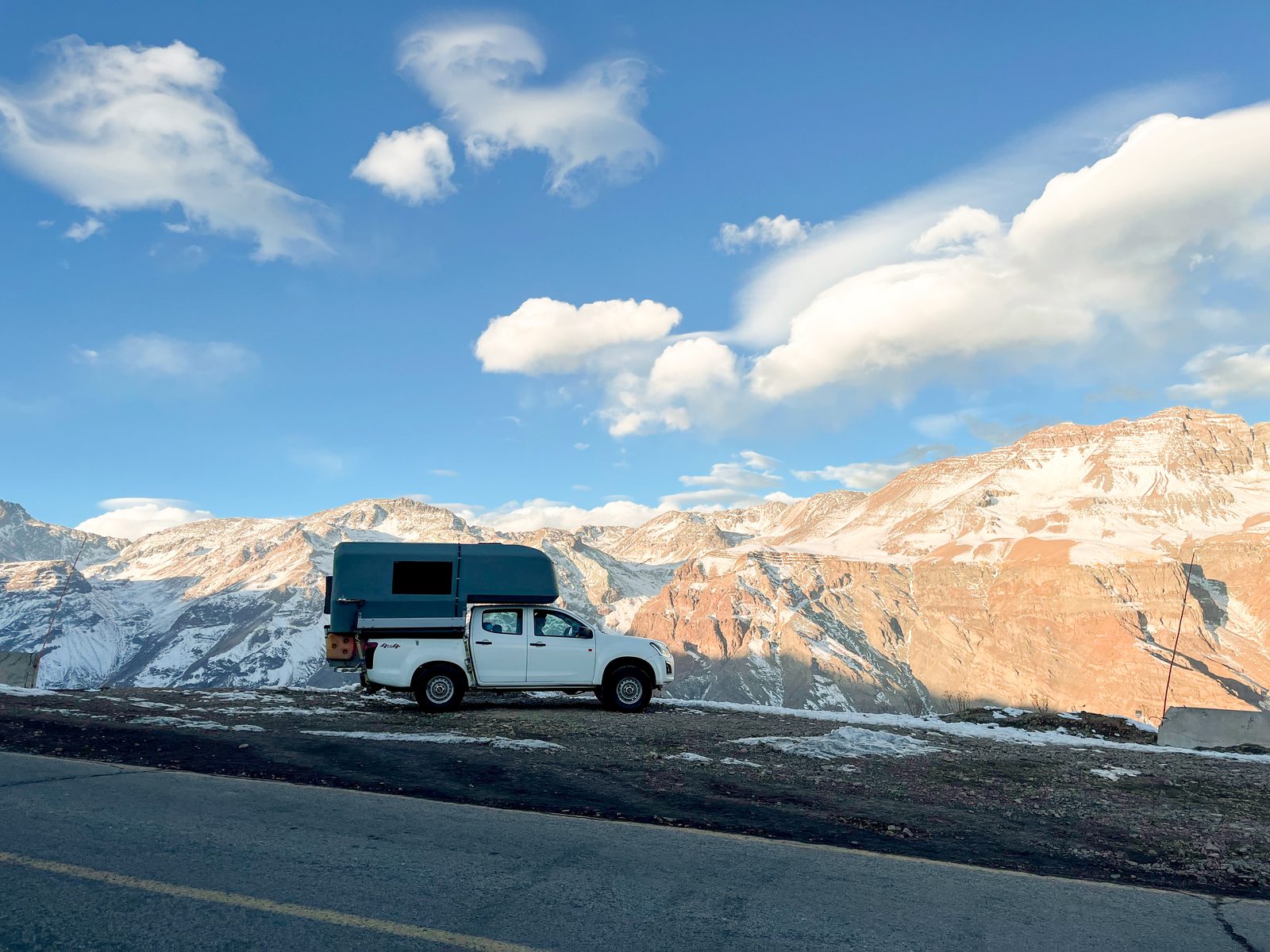 4x4 camper truck at a mountain viewpoint at sunset, snow-covered peaks behind