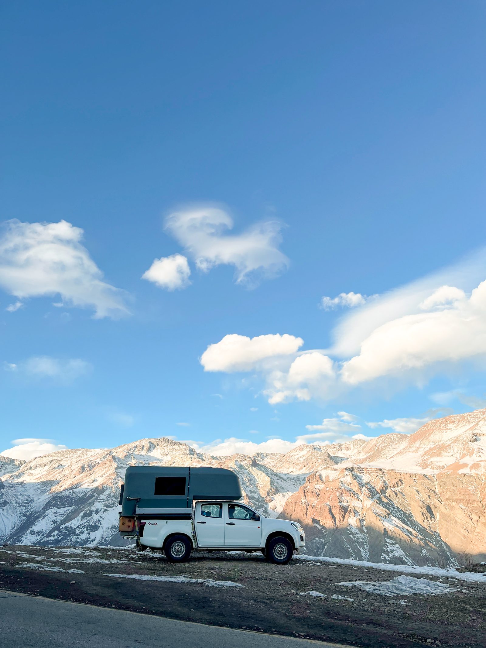 4x4 camper truck parked at a mountain viewpoint with snow-covered peaks