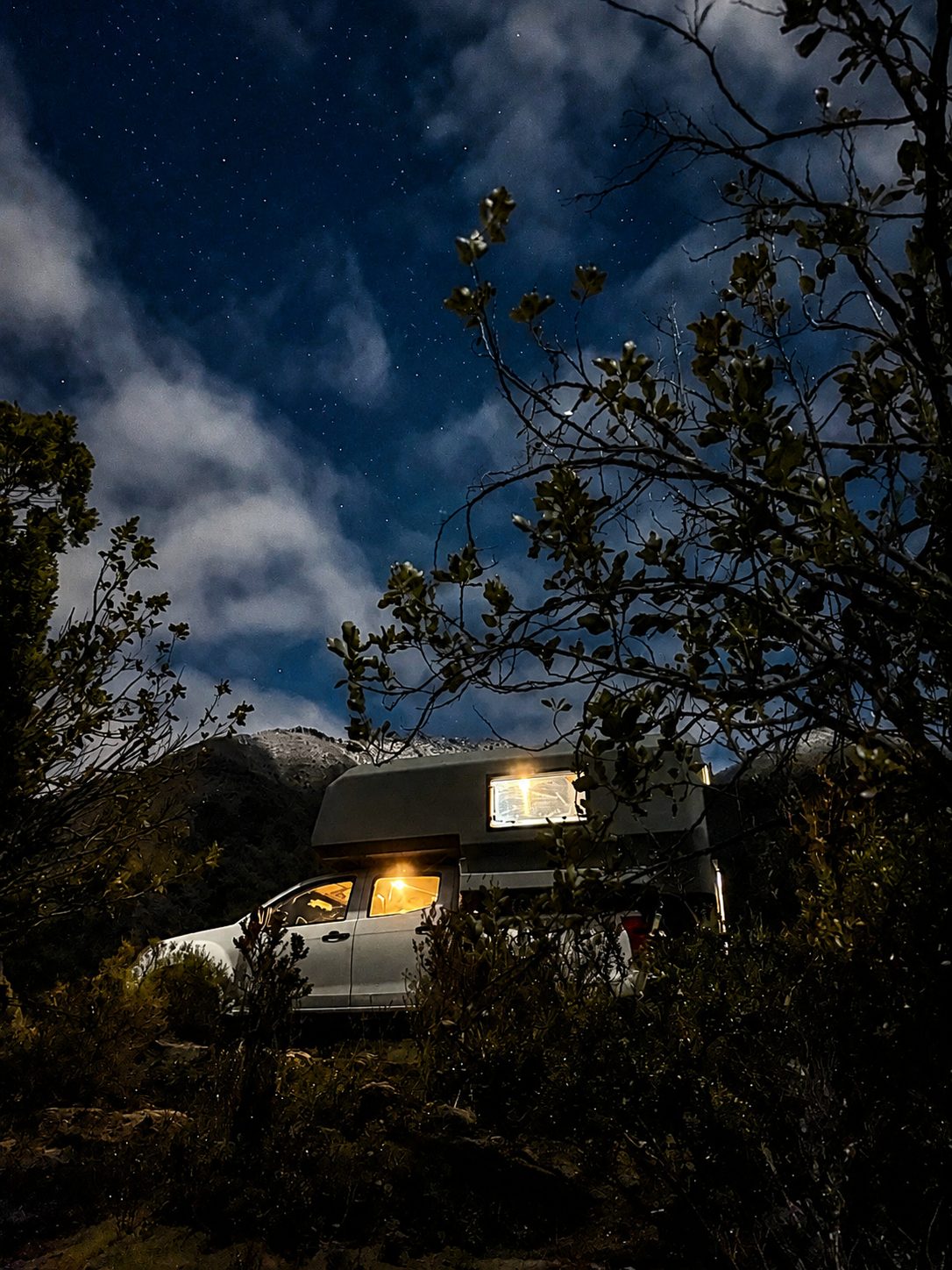 Camper truck 4x4 de noche bajo un cielo estrellado con la luz interior encendida