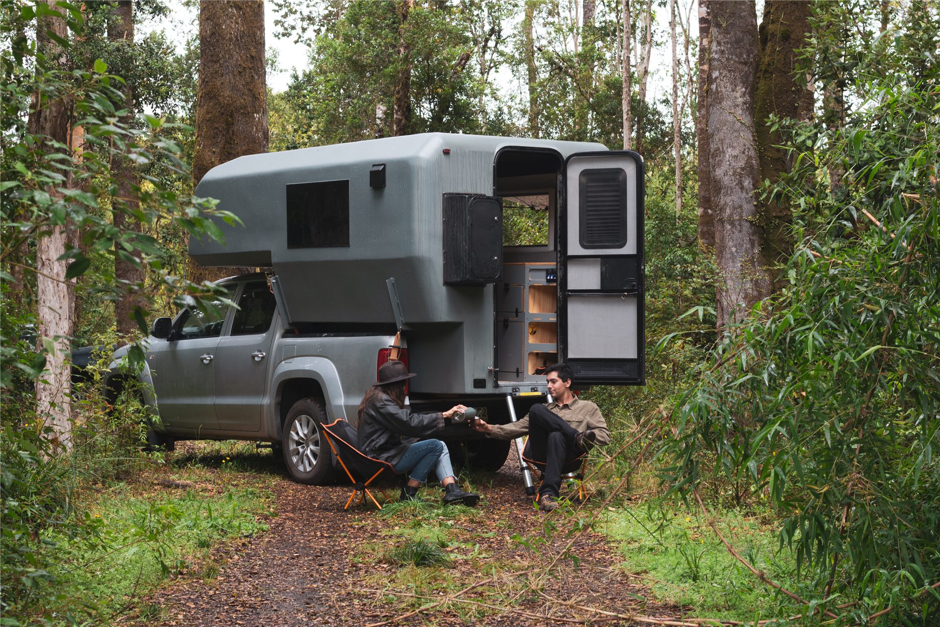 Couple sitting outside a camper truck with camping chairs in the forest