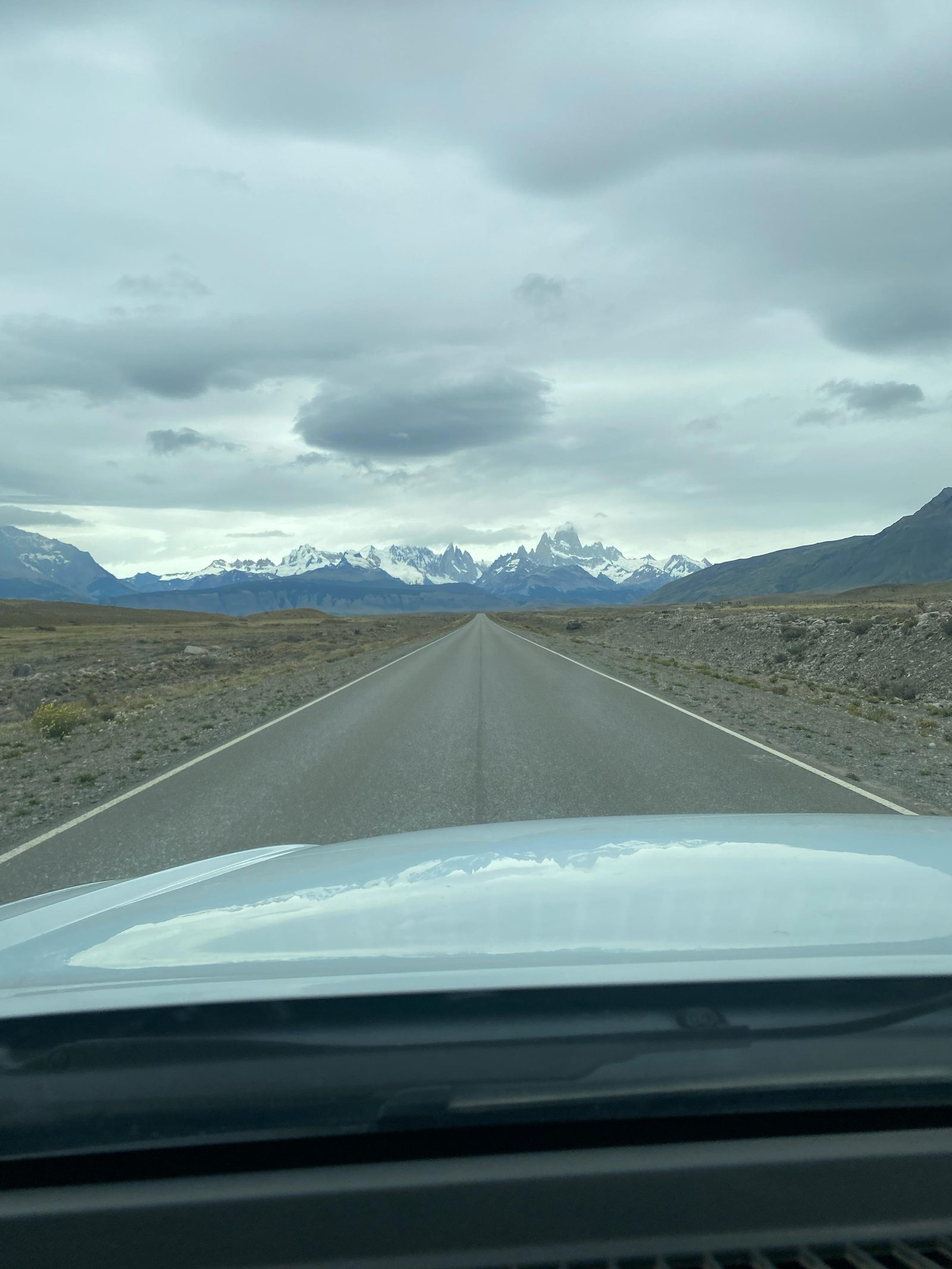 Straight road in Argentine Patagonia seen from inside the camper, snow-covered mountains ahead